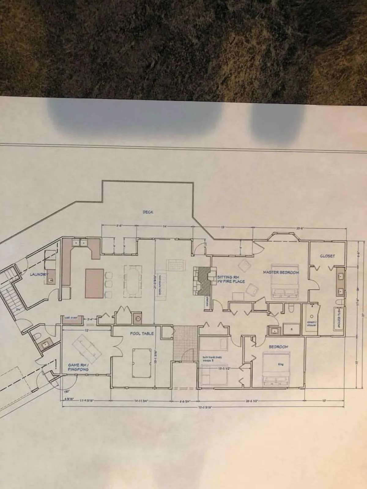 An open plan that visually connects a master bedroom, a sitting room with a fireplace, a game room, and a deck. The scene captures multiple communal spaces, each inviting for relaxation, games, and evening gatherings, illustrating how these hubs flow seamlessly together.