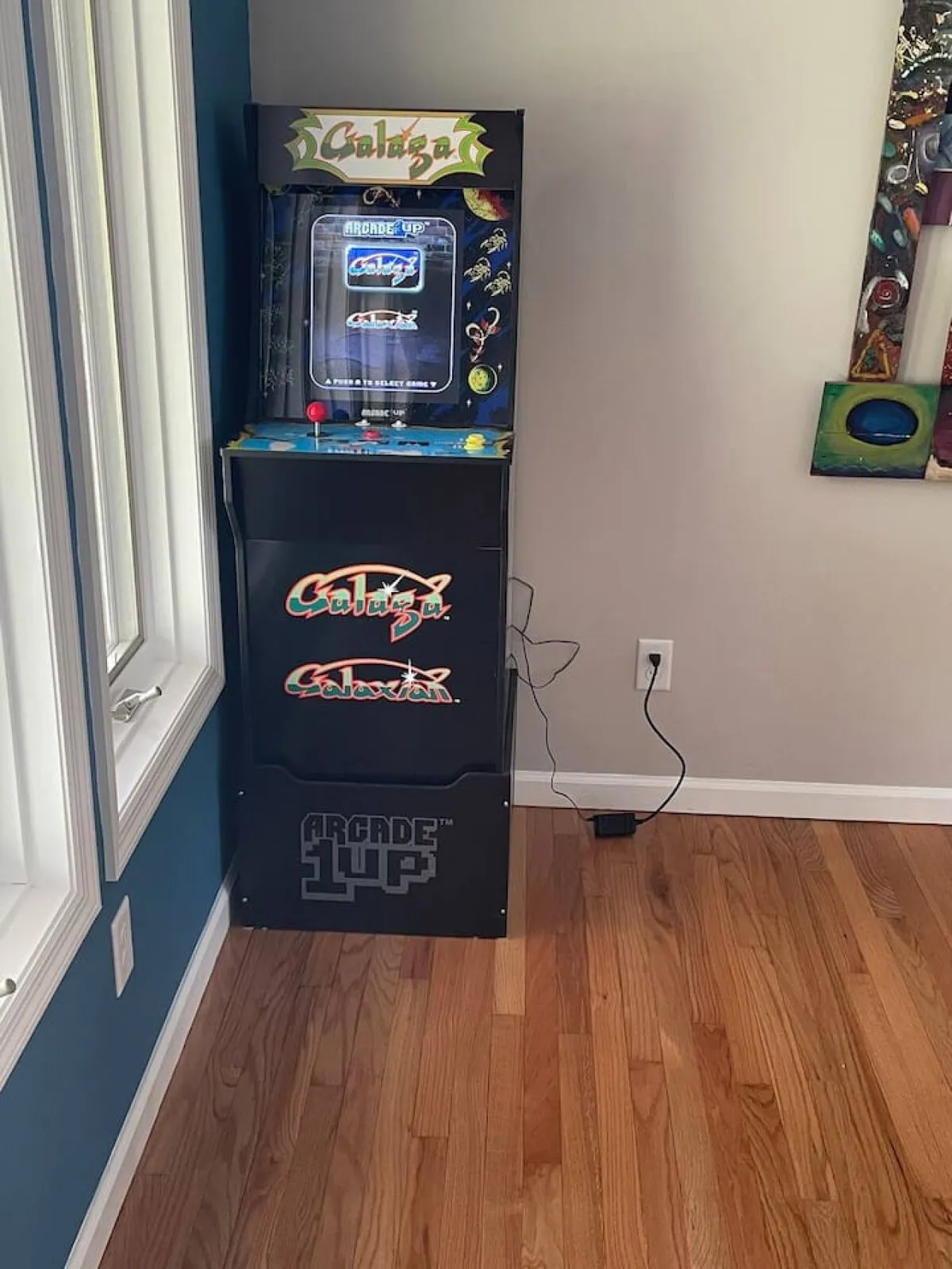 A vibrant game room featuring a classic arcade machine, wooden flooring, and a bold blue accent wall, offering a lively spot for friendly competition and socializing.