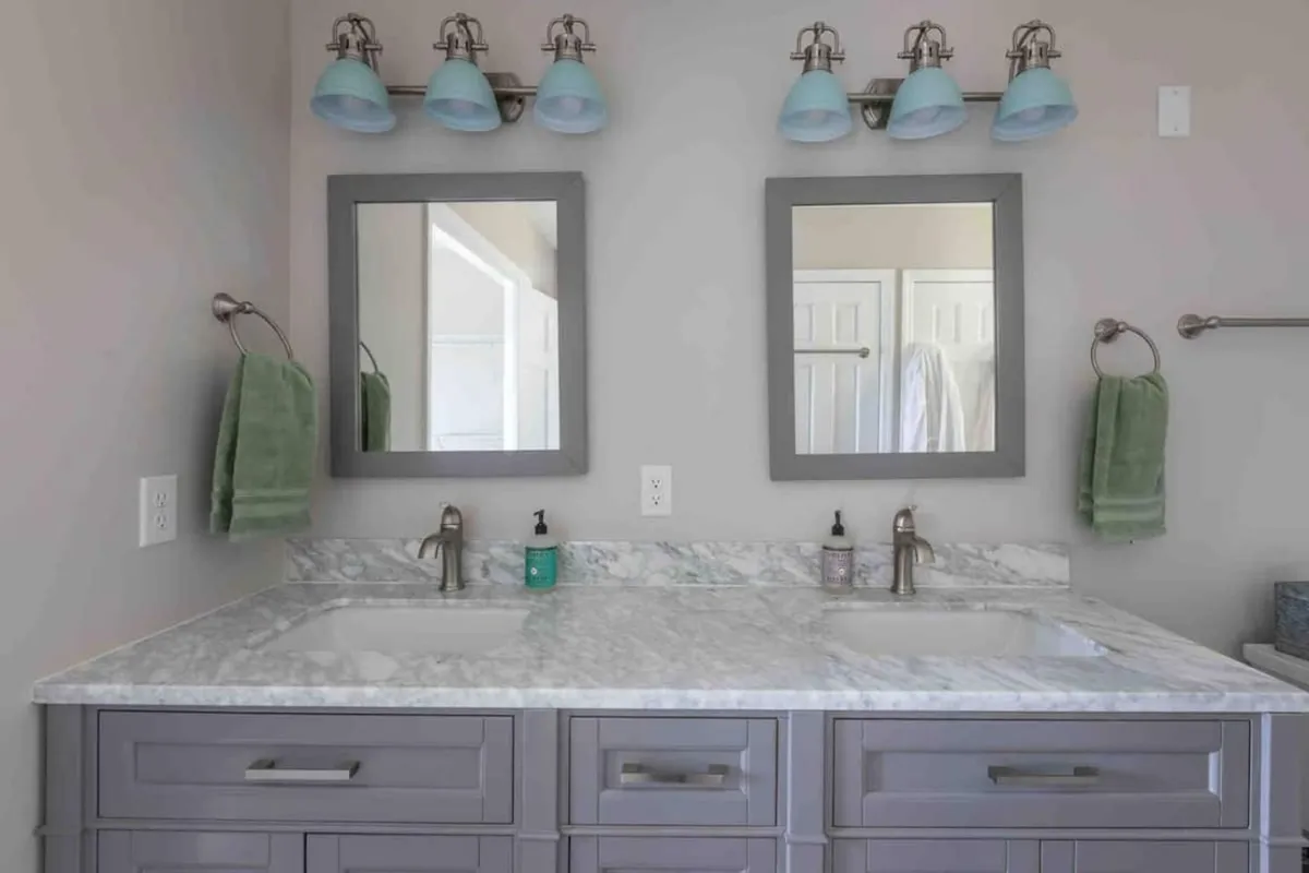 A modern bathroom with a double sink set in a marble countertop, two mirrors, and elegant light fixtures. The space exudes calm with its clean lines and uncluttered surfaces, ideal for morning and evening routines.