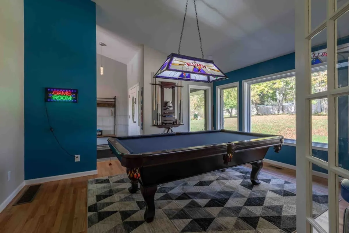 A vibrant game room featuring a classic pool table, a stained glass chandelier, and a 'game room' sign. The room is set up for friendly competition and leisure, with space for socializing and celebrating with friends and family.