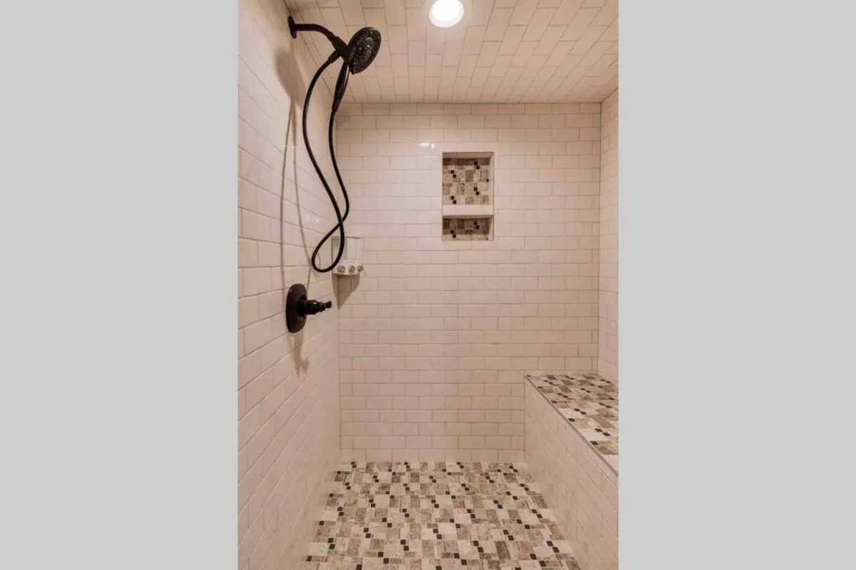 This image features a luxurious shower area with a prominent showerhead, built-in shelf, bench seating, and stylish mosaic tile flooring. The scene evokes a calm and rejuvenating atmosphere, suggesting a spa-like environment within the home.
